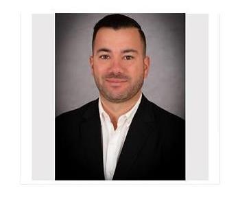 White male in front of background with black suit jacket and white button up shirt