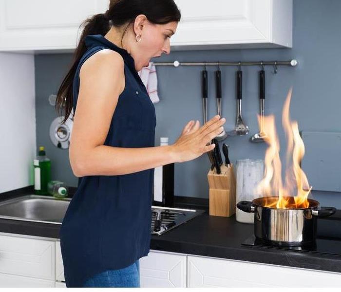 A closeup of a woman in shock as her cooking pot catches fire