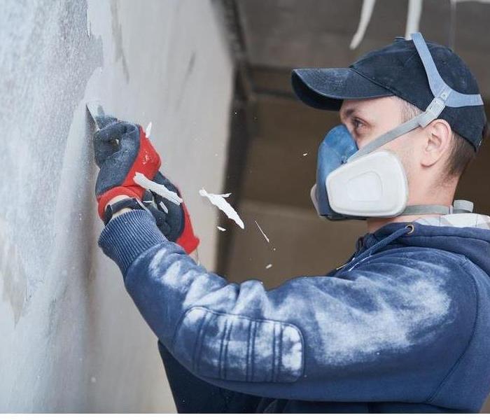 A worker in a mask removing soot from a wall using a special tool