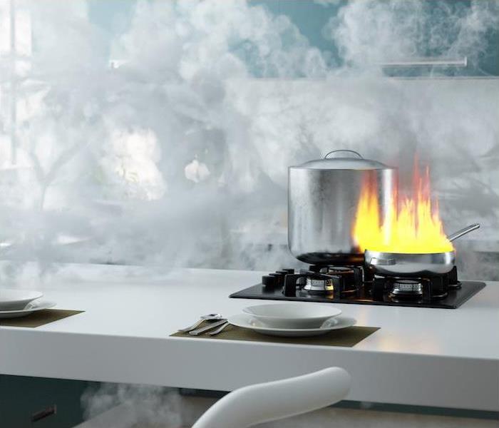 Steel pan on a gas cooktop on top of a kitchen counter that is ablaze with a grease fire and surrounded by smoke
